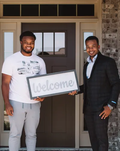 Teré with a buyer holding a Welcome sign at his new front door