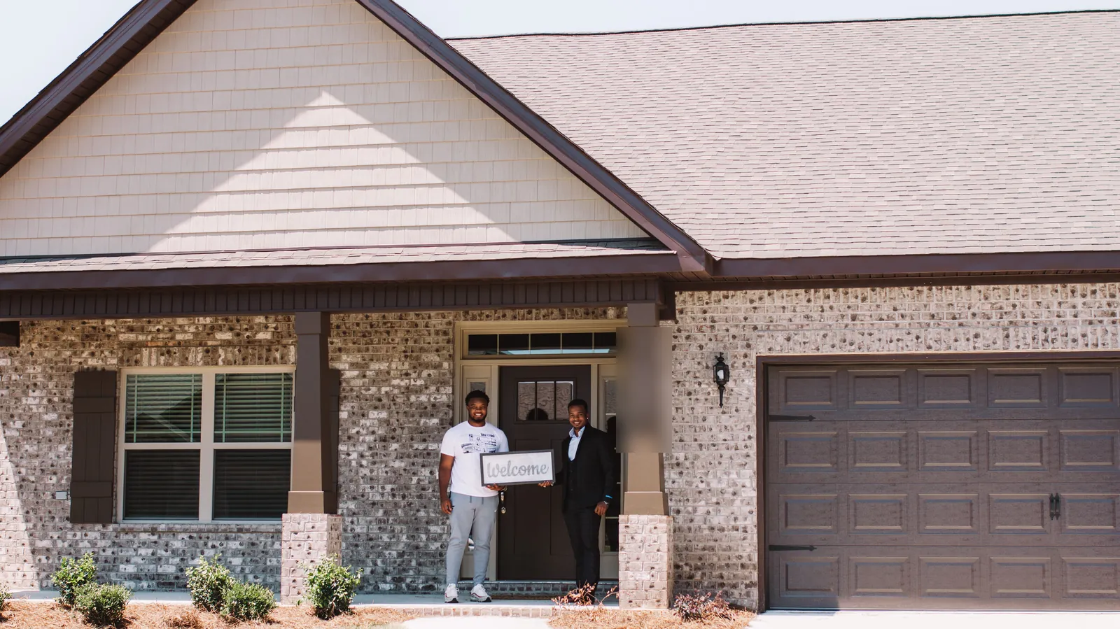 Teré Calloway with a buyer holding a Welcome sign at a new-construction home